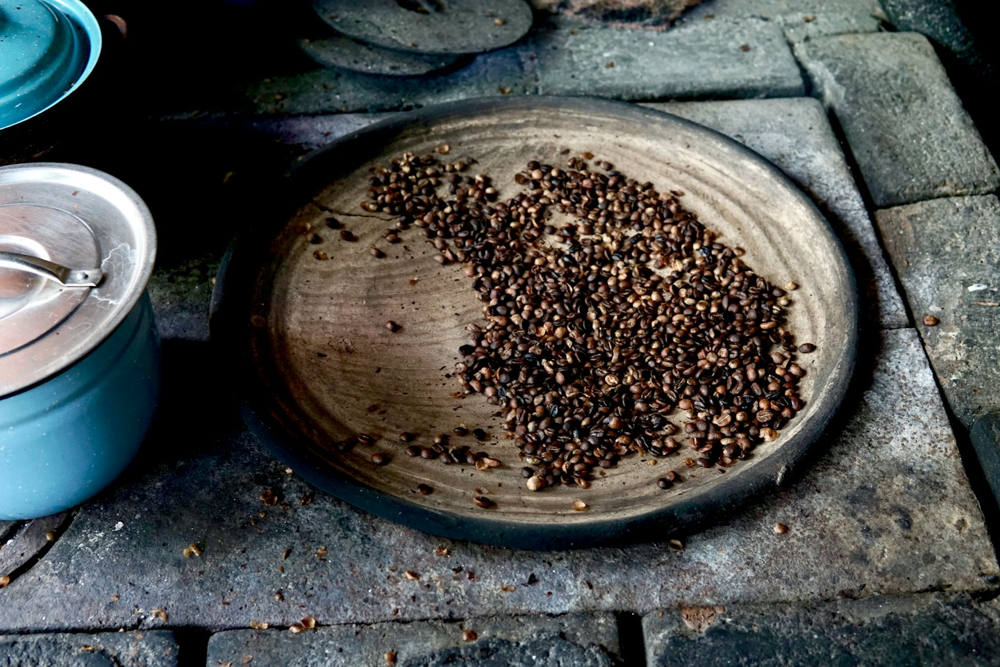 Rostade kaffebönor på en träbricka bredvid två krukor.